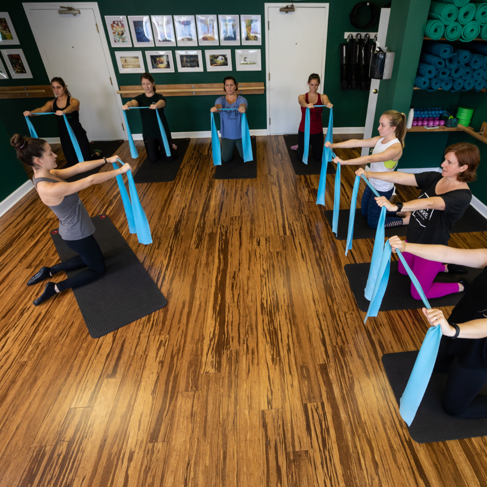women on thick yoga mats in low-impact mat barre class exercising arms contracting core using therabands with instructor