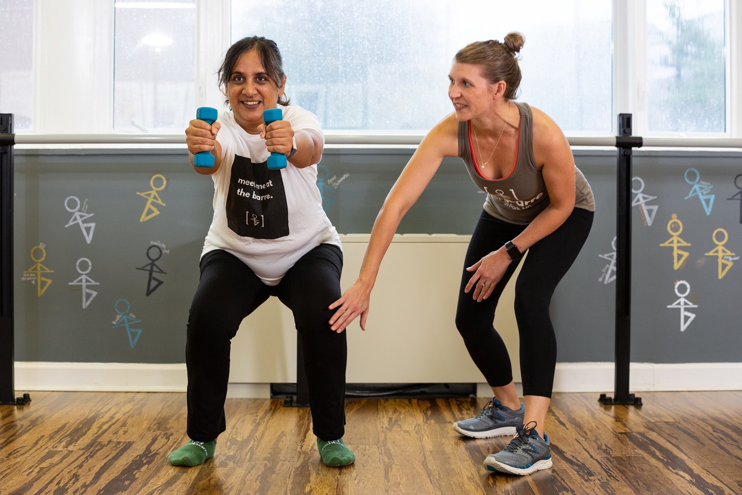 group of women squatting in clean fitness studio receiving hands on adjustment from instructor
